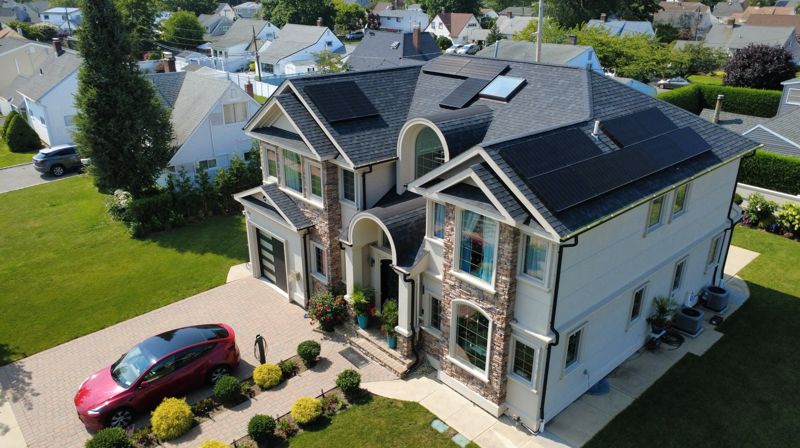 Drone photo of a two-story stone and siding home with solar panels in Hicksville, NY